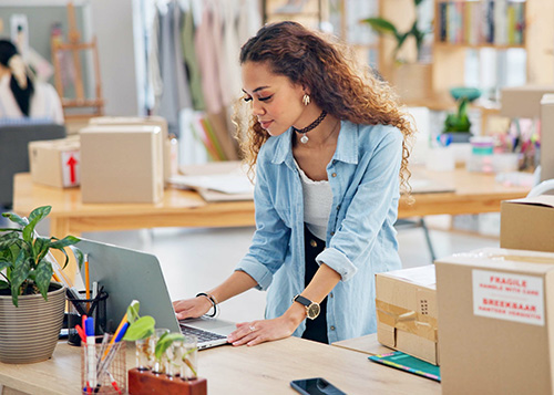 women standing at desk, working on computer in shipping room